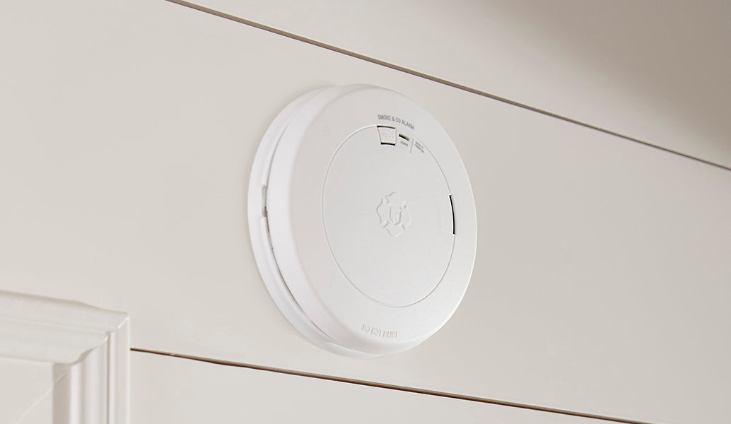 A white circular wireless smoke detector mounted on a white shiplap wall.