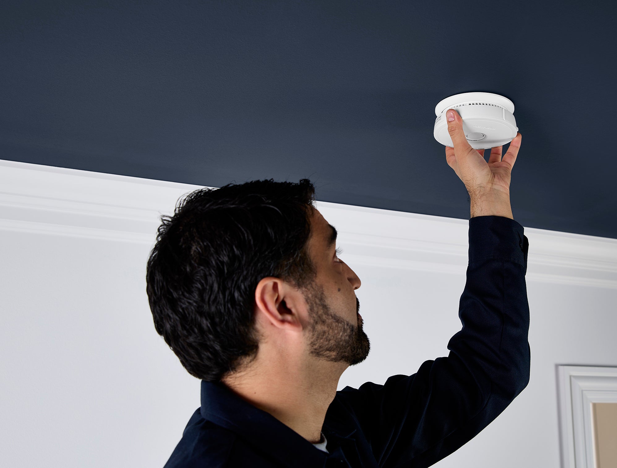 Person installing a ceiling-mounted smoke alarm inside a residential room.