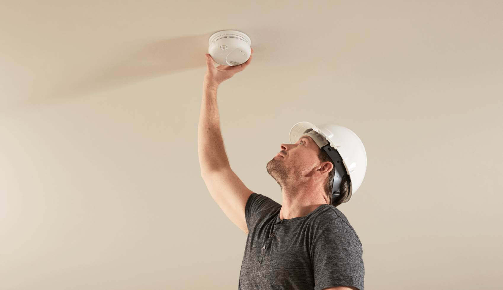 A professional installer installs a smoke alarm on a ceiling.