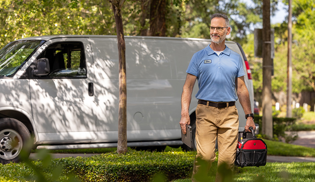 A professional technician, carrying tools and computer is leaving his utility van to work.